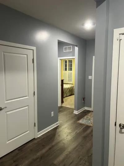Gray hallway with plank flooring and white doors leading to a yellow bedroom with plantation shutters
