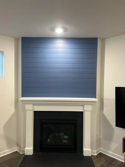 Basement gas fireplace with white mantel below a blue shiplap accent wall and recessed light.