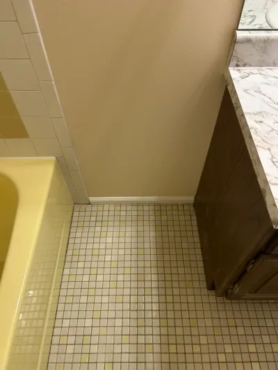 Dated bathroom corner with gold tub, cream mosaic tile floor and dark wood vanity before remodeling