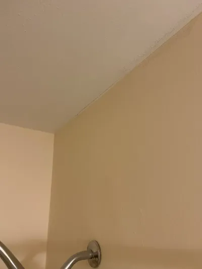 Bathroom corner showing a cracked seam where the textured ceiling meets a beige wall above a shower arm.