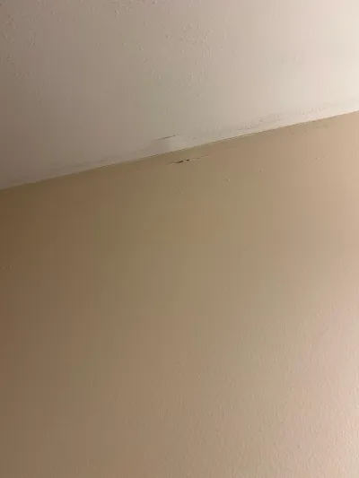 Cracked drywall seam where a beige wall meets a white textured ceiling, with tape separation visible.