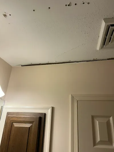 Bathroom ceiling corner with a crack, nail holes, and a gap where trim was removed above two doors.