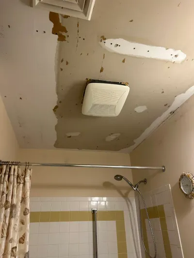 Bathroom ceiling with peeling paint and patching above a white tiled tub shower with chrome fixtures.
