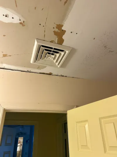 Peeling, cracked hallway ceiling around a square HVAC register above an open paneled door.