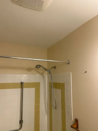 Dated bathroom shower alcove with white and gold striped tile, chrome grab bar and handheld shower head.
