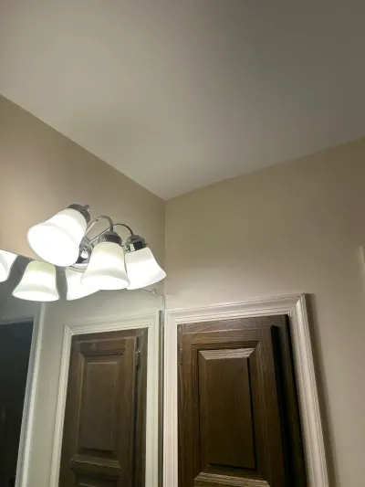 Chrome vanity light with frosted shades on a beige wall beneath a sloped ceiling, beside a dark wood door.