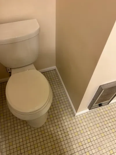 White toilet in a corner above a cream and yellow square mosaic tile floor with beige walls.