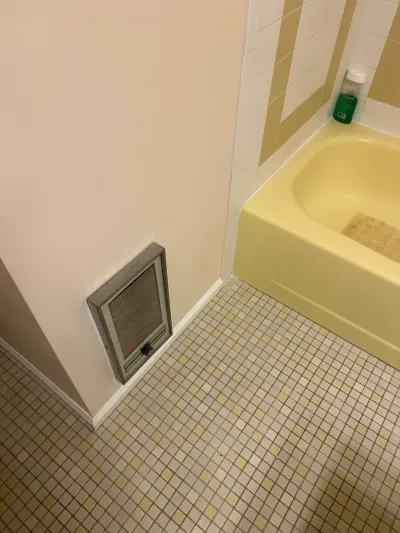Corner of a dated bathroom with a yellow alcove tub, tiled surround, and yellow-and-cream mosaic tile floor.