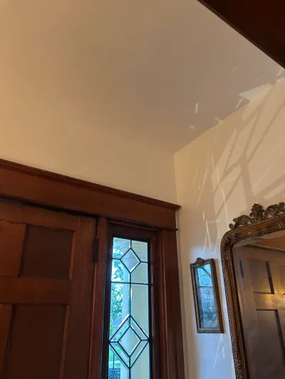 Foyer corner with dark wood door, leaded glass sidelight, and gilt-framed mirrors under white ceiling.