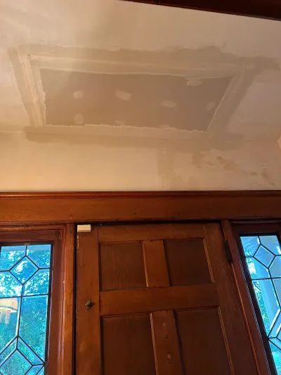 Freshly patched ceiling drywall above a stained wood entry door with leaded glass sidelights.