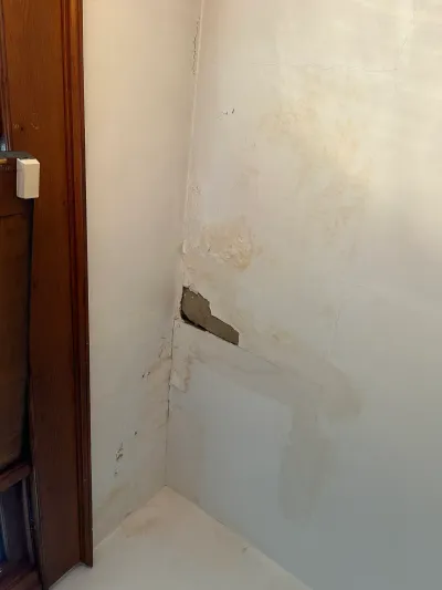 Water-stained and cracked plaster wall corner with missing plaster beside dark stained wood door trim.