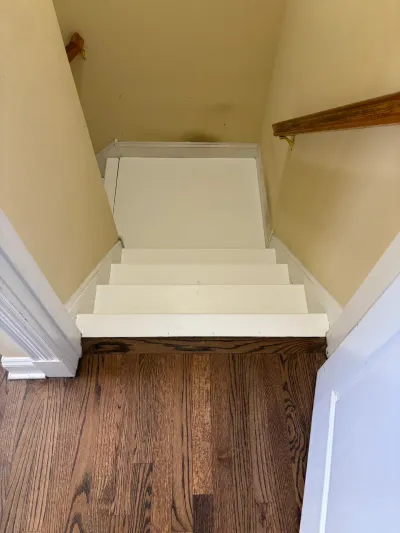 Narrow staircase with white painted treads and risers rising from a brown oak hardwood floor to a landing.