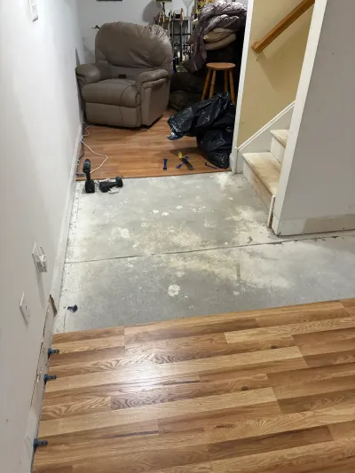 Basement laminate plank flooring partly installed over bare concrete, with tools and debris bags nearby.