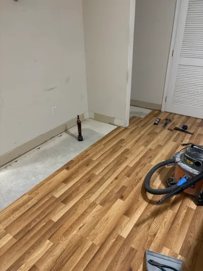 Room mid-remodel with light oak plank flooring partly installed over bare concrete and tools nearby.