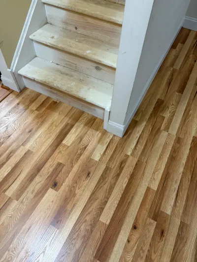 Newly installed oak hardwood floor meeting a staircase with stripped bare wood treads and white trim.