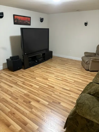 Finished basement rec room with light oak laminate floors, big-screen TV, recliner and green sofa.