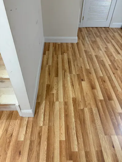 Newly laid unfinished red oak strip flooring in a white hallway beside louvered bifold closet doors.