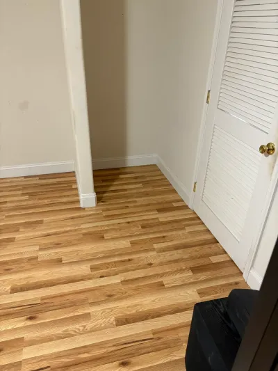 Corner of a room with new natural oak flooring, white baseboards, and a white louvered closet door with brass knob.