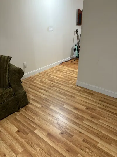 Living room with new honey oak plank flooring, greige walls, white baseboard, and an olive armchair.