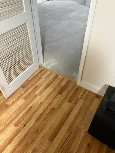 Light oak plank flooring meeting a wood threshold at a doorway opening onto a bare concrete garage floor.