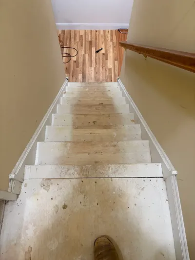 Straight staircase with carpet removed, exposing bare treads, white risers and new oak floor at the landing.