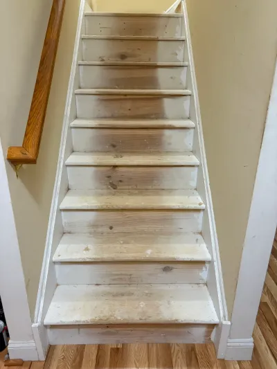 Straight staircase with carpet removed, showing bare wood treads, white risers and an oak handrail.