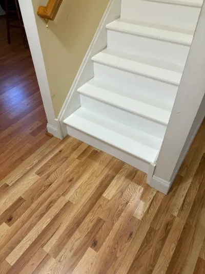 White painted staircase meeting newly installed natural oak hardwood flooring in an entry hall.