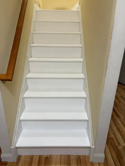 Narrow straight staircase with freshly painted white treads and risers, oak handrail, and oak floor below.