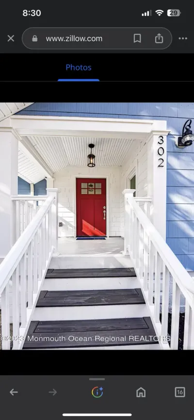 Red front door under a white covered porch with black pendant light, reached by white steps with railings.