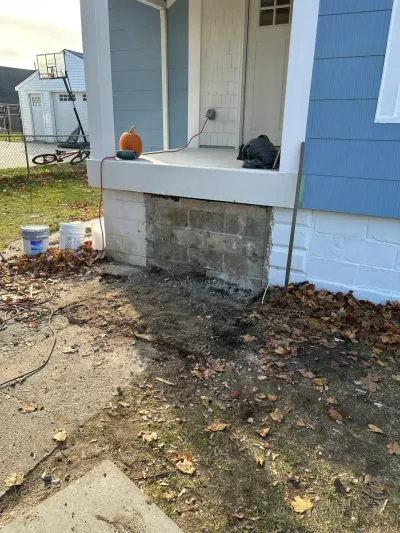 Front porch corner with exposed block foundation and excavated soil during exterior repair work.