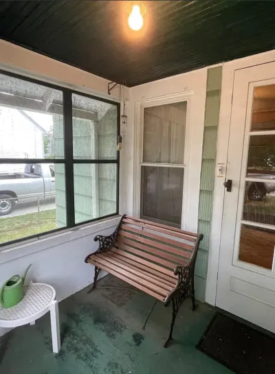 Enclosed front porch with green painted floor, dark beadboard ceiling, slat bench and screened openings.