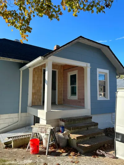 Blue-sided house with white-columned front porch being re-clad in fresh cedar shake shingles.