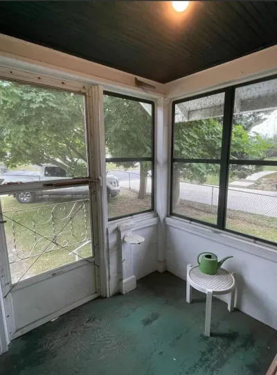 Enclosed porch with dark green beadboard ceiling, worn teal painted floor, and corner banks of windows.