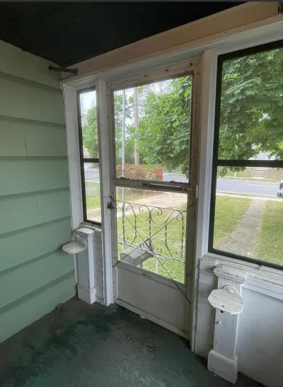 Enclosed porch with mint green siding wall, teal floor and white screen door with iron scrollwork before renovation