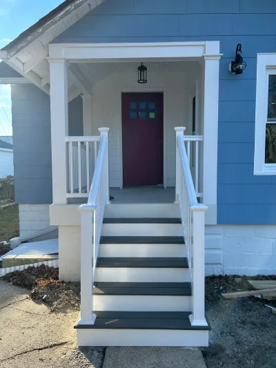 Blue-sided home's white front porch with gray composite steps, white railings and a burgundy front door.