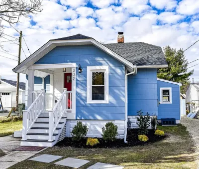 Blue bungalow with white trim, red front door, covered porch and new mulched foundation plantings.