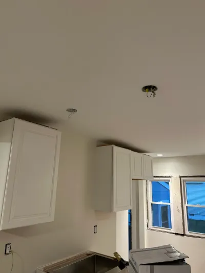 Kitchen mid-remodel with white raised-panel upper cabinets, hanging ceiling wiring and an unfinished sink counter.