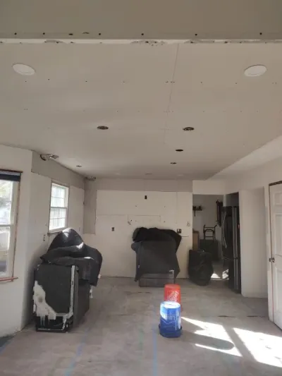 Gutted kitchen mid-renovation with bare drywall, roughed-in recessed lights and covered appliances.