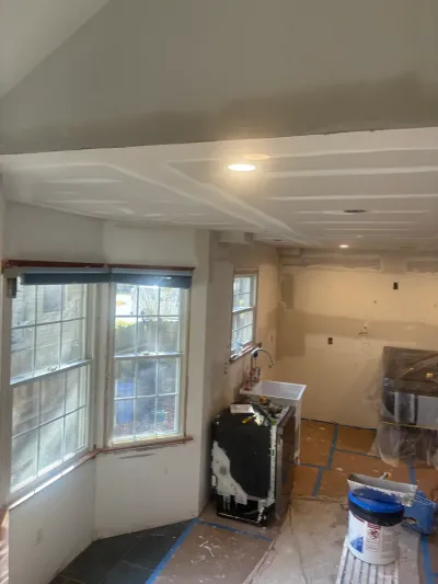 Kitchen under renovation with fresh taped drywall, recessed lights, sloped ceiling and covered tile floor.