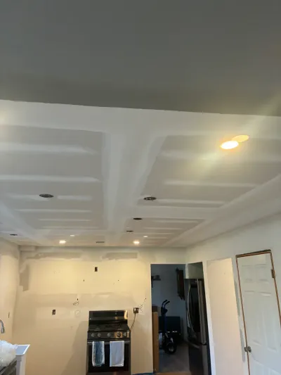 Kitchen mid-remodel with freshly mudded drywall ceiling, recessed light cans, bare walls, and a stainless range.
