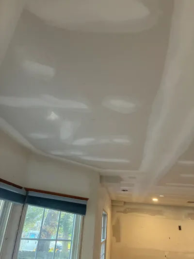 Drywall ceiling with a tray recess and soffit, taped and mudded, with one recessed light lit above taped windows.