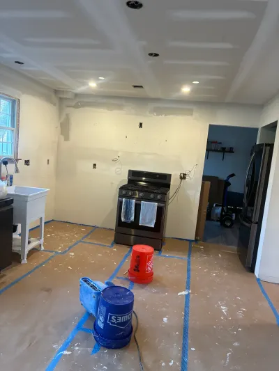 Kitchen mid-remodel with bare taped drywall, recessed lights, paper-covered floor, range and refrigerator in place.
