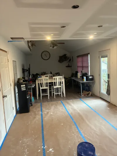 Open living and dining space mid-remodel with new drywall ceiling, recessed lights and papered floor.