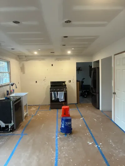 Gutted kitchen mid-remodel with bare drywall, rosin paper floor, range and refrigerator still in place.