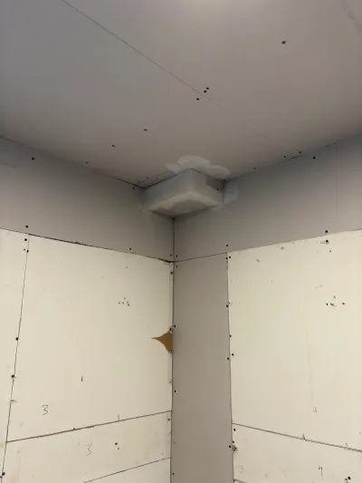 Bathroom corner under construction with backer board walls, drywall ceiling and a roughed-in exhaust fan