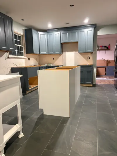 Kitchen under renovation with blue raised-panel cabinets, gray tile floor, and an island awaiting countertops.