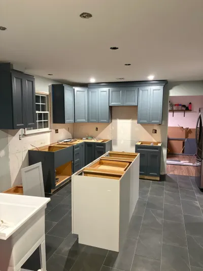 Kitchen under construction with blue-gray cabinets, no countertops, white island frame and gray tile floor.