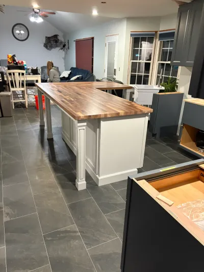 Kitchen mid-remodel with butcher block island, white island base, dark gray shaker cabinets and gray tile floor