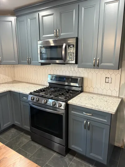 Gray-blue kitchen cabinets with speckled stone counters, cream picket tile backsplash and stainless range.