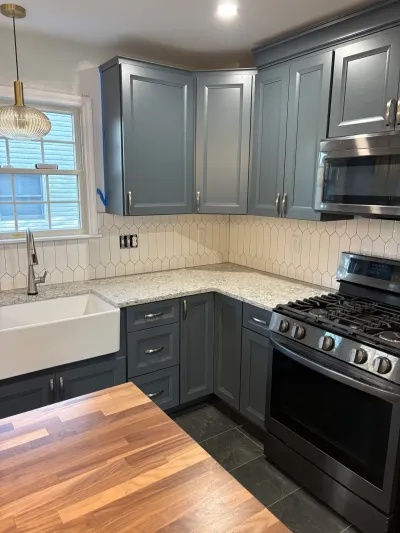 Blue-gray raised-panel kitchen with granite counters, farmhouse sink, picket tile backsplash and butcher block island.